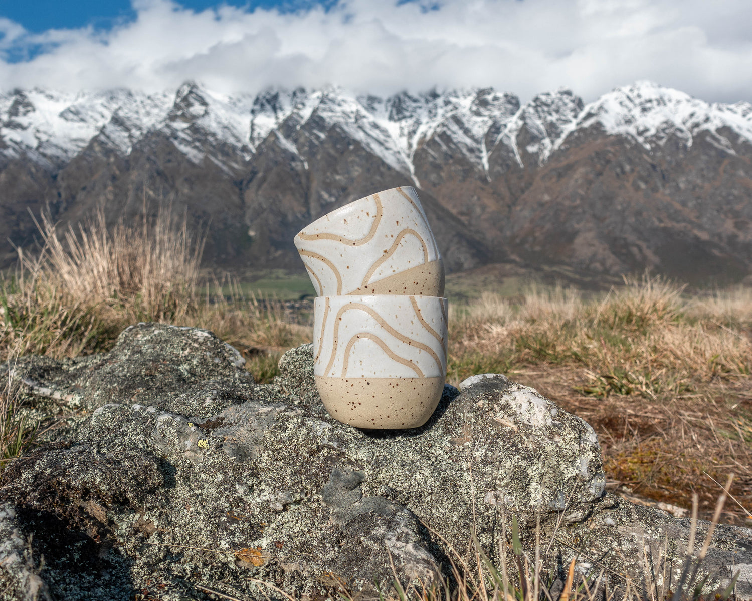 handleless coffee mug tumbler with abstract topographic line art glaze design with mountains behind handmade in New Zealand by land and line ceramics