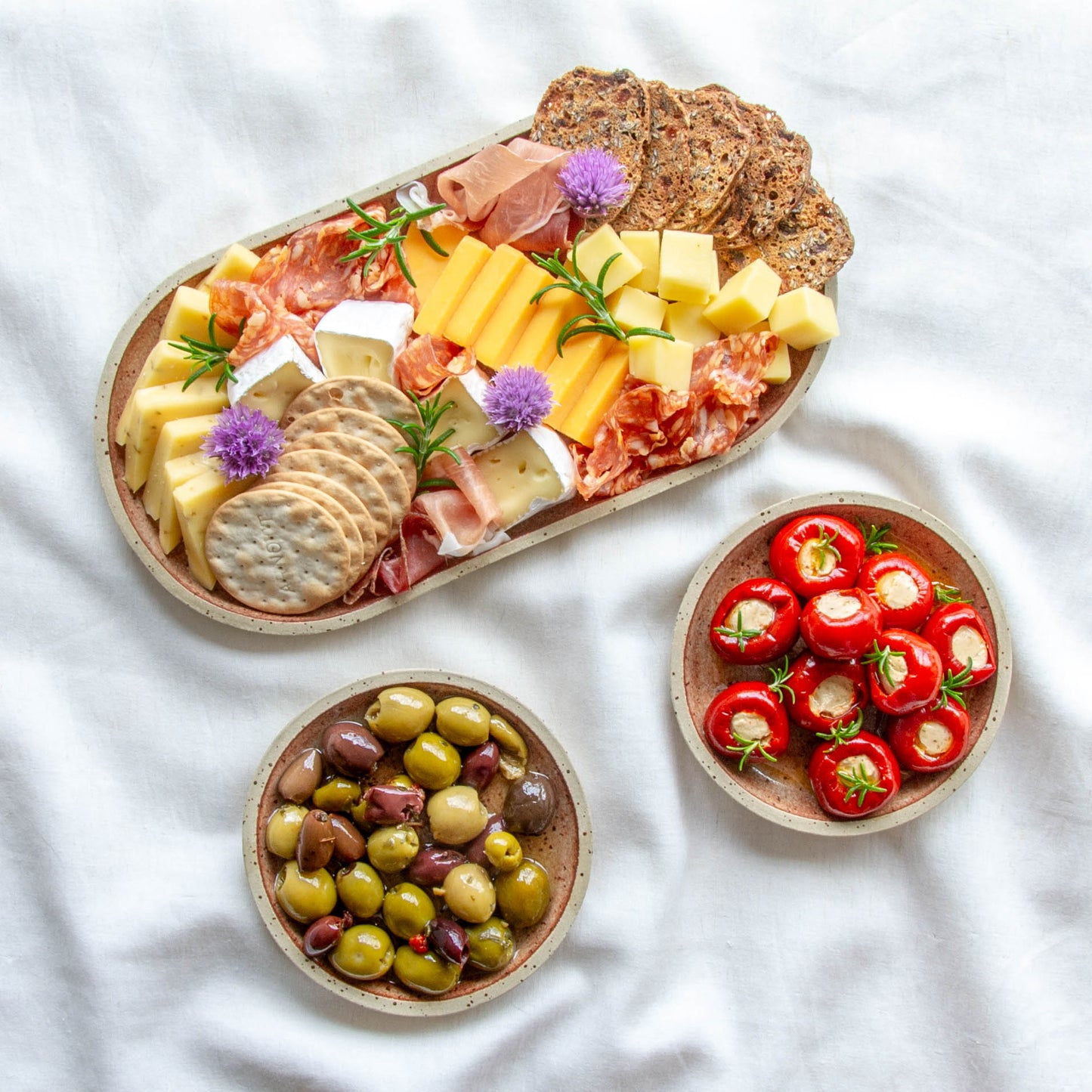 handmade ceramic cheese board. rounded oblong pill shaped platter and matching small side plates with charcuterie and olives