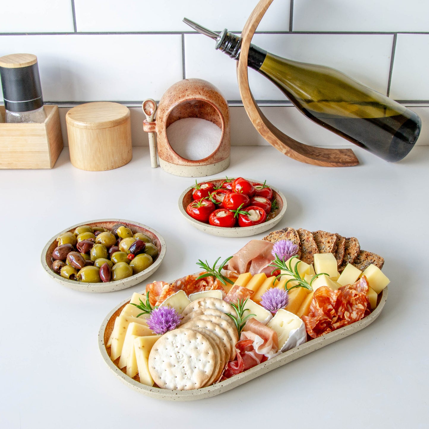 rounded oblong, pill shaped plate with cheese and charcuterie small side plates with olives and stuffed peppers